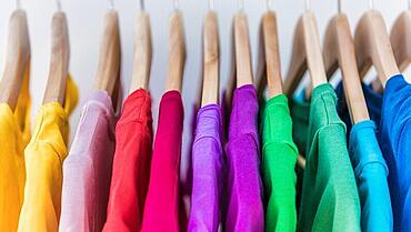 Fashion clothes on clothing rack - bright colorful closet. Closeup of rainbow color choice of trendy female wear on hangers in store closet or spring cleaning concept. Summer home wardrobe.