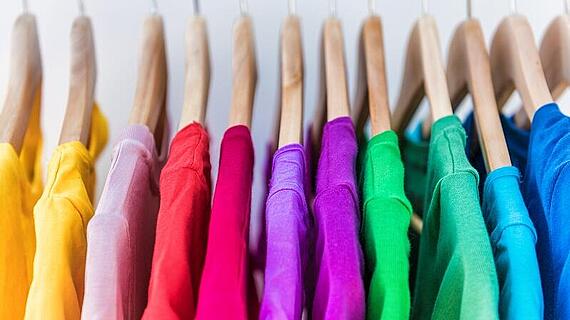 Fashion clothes on clothing rack - bright colorful closet. Closeup of rainbow color choice of trendy female wear on hangers in store closet or spring cleaning concept. Summer home wardrobe.